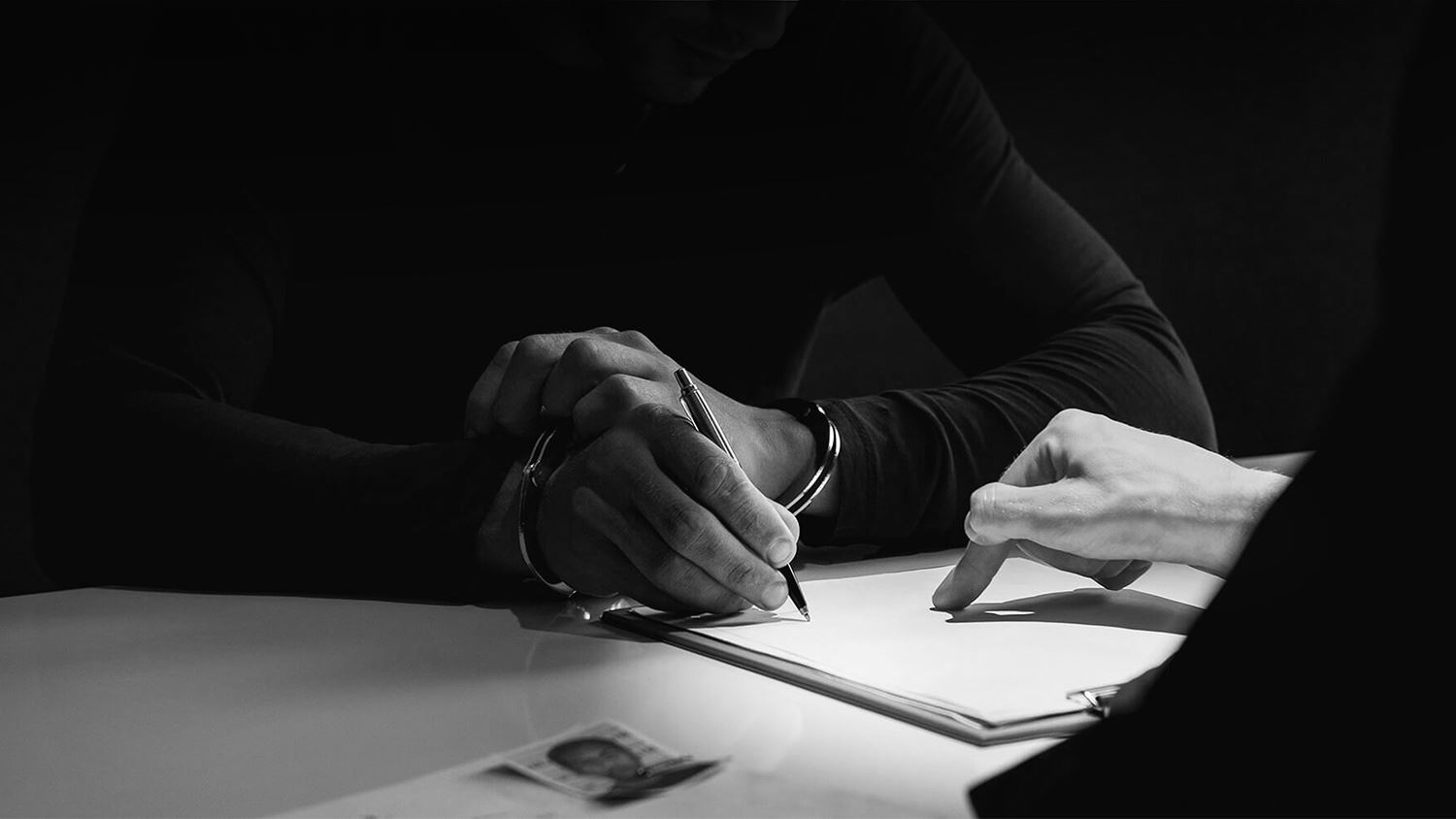 person signing paperwork in handcuffs